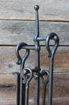 fire tool loop and scroll handles on a stand against a wooden wall 
