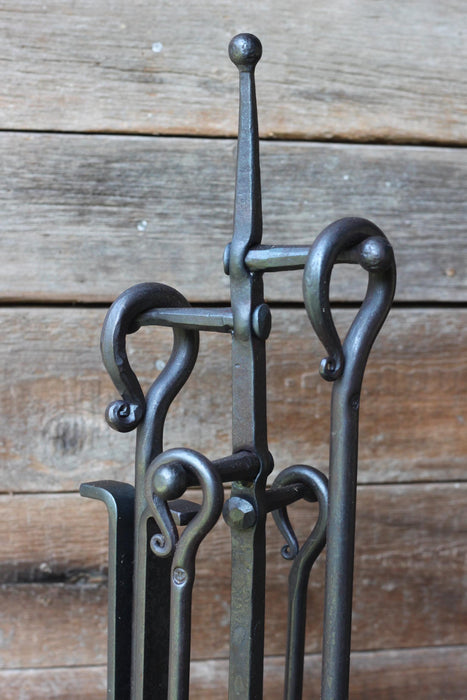 fire tool loop and scroll handles on a stand against a wooden wall 