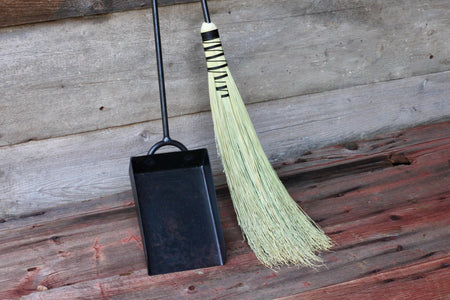 hand woven fire broom and wrought iron shovel set by wicks forge against a wooden wall 