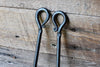 looped scroll handles of the broom set against a wooden wall by wicks forge 
