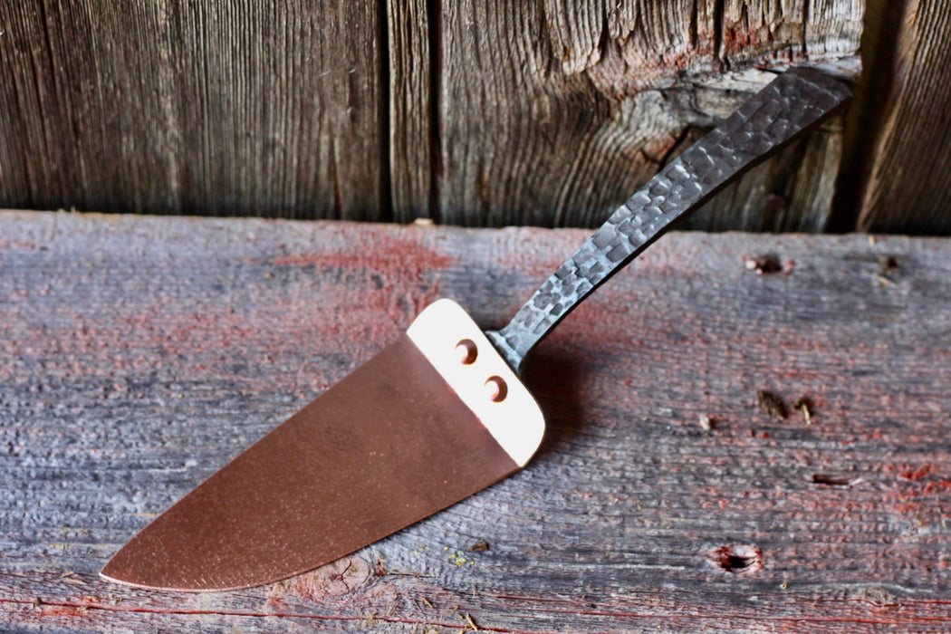 cake slicer made of brass and iron on a wooden surface by wicks forge 