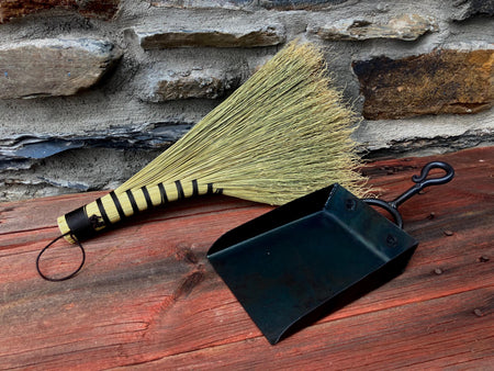 a hand made hand broom and shovel against a rustic wall and table background by wicks forge 