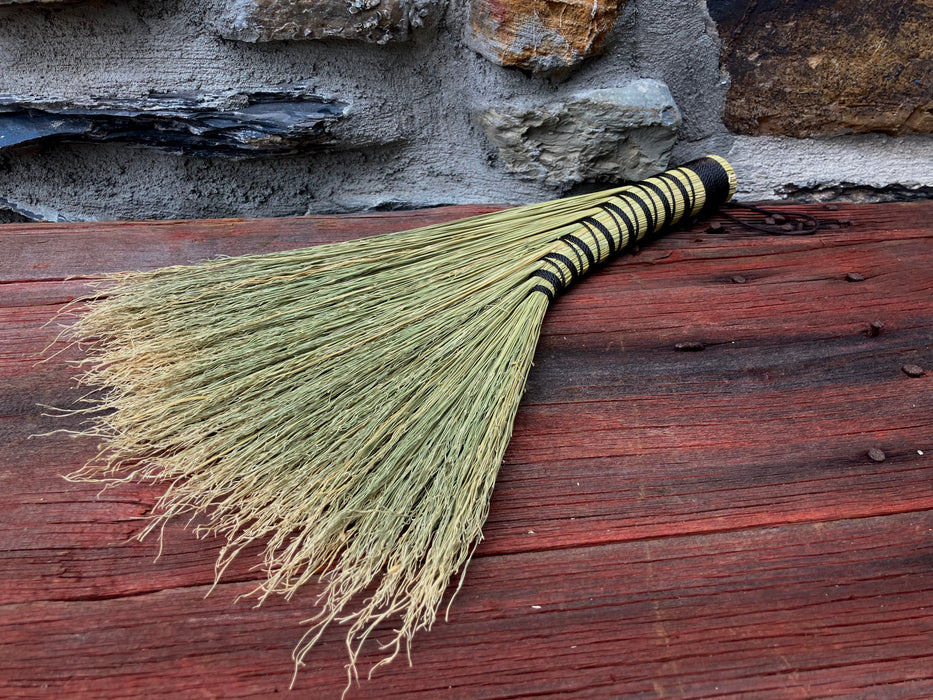 a yellow broom on a wooden table and rustic stone wall in the background by wicks forge 