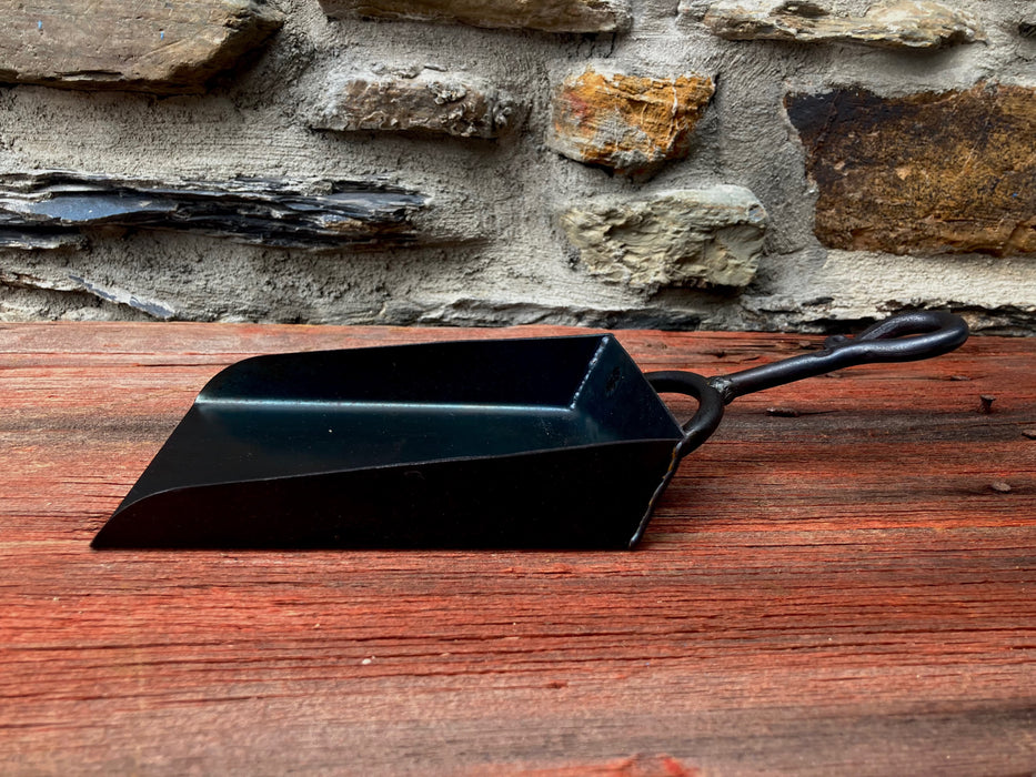 a black shovel on a wooden table and stone wall in the background 