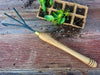 garden fork with long wooden handle and basil plants in a punnet on a wooden surface 