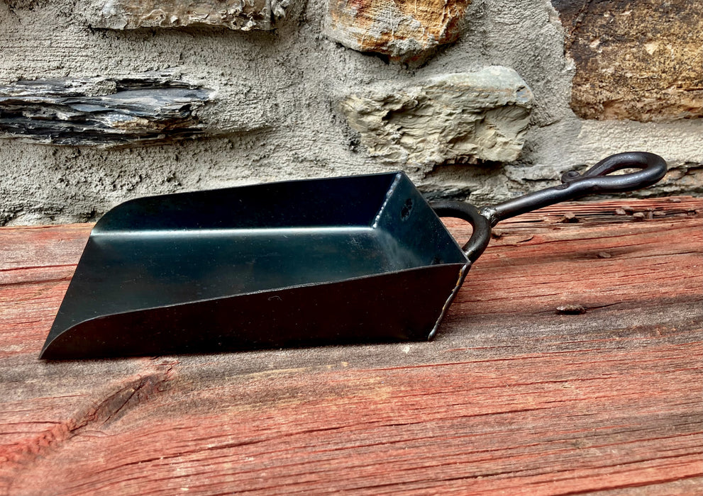 a black hand shovel on a wooden table and stone wall in the background 
