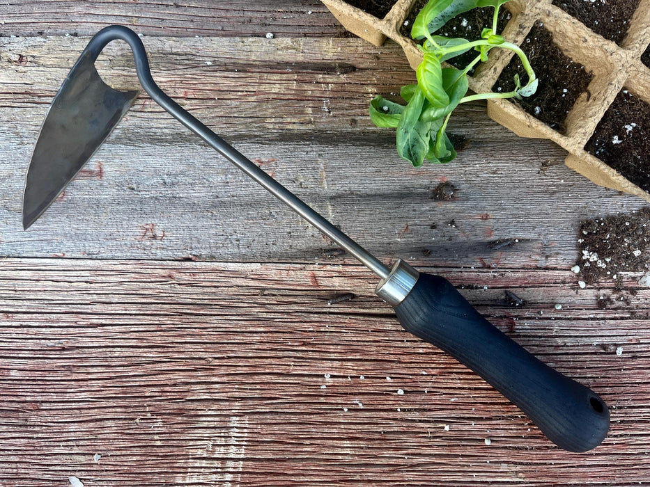 Gardening tool with a black handle on a wooden surface next to a small plant in a seed tray.