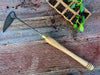 Gardening tool with wooden handle on a wooden surface with soil and plants.