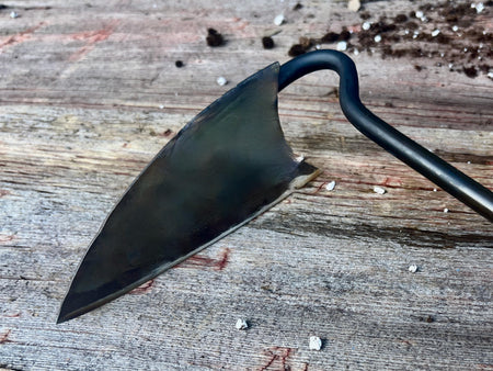 the main part of the garden weeder on a wood surface with soil debris in the background by wicks forge 