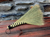 a hand woven broom against a rustic wall on a wooden table by wicks forge 