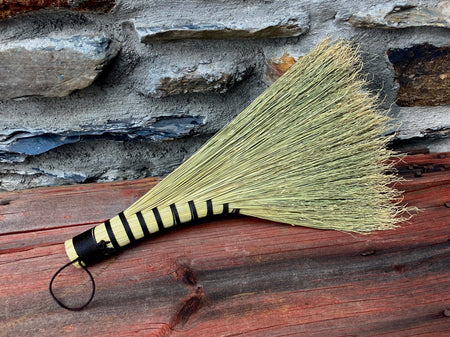 a hand woven broom against a rustic wall on a wooden table by wicks forge 