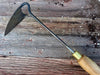 long handle garden weeder with a wooden handle against a soiled wooden surface by wicks forge 