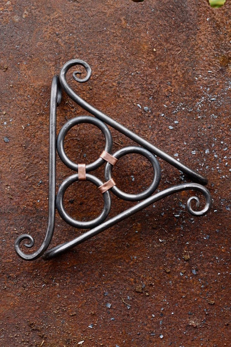 a hand forged blacksmith trivet with copper wrapping and a scroll detail by Wicks Forge