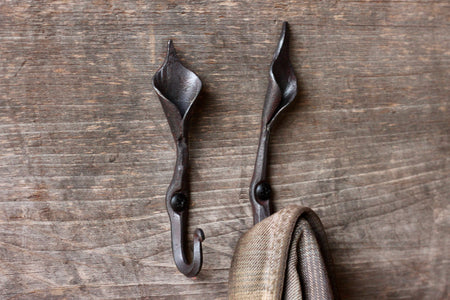 iron Lilly wall hook with a coat hanging on it on a wooden wall 