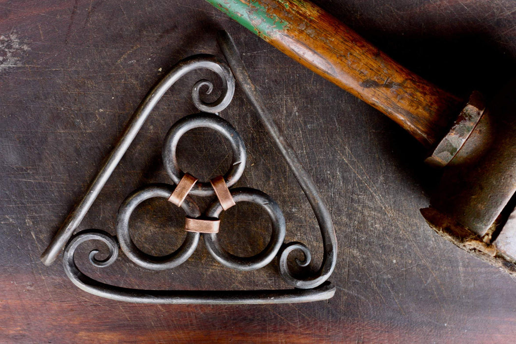 a blacksmith hand forged copper wrapped trivet with an inside scroll design by Wicks Forge