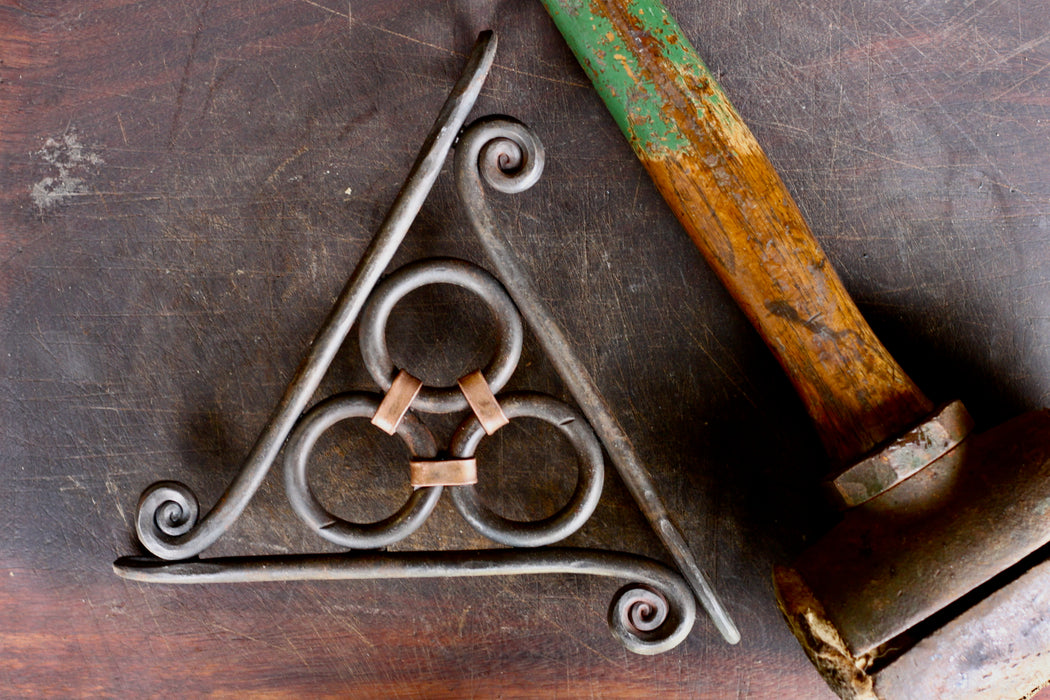 a blacksmith hand forged copper wrapped trivet with a fiddlehead detail by Wicks Forge