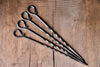 A set of 4 hand forged Skewers on a rustic wooden surface made by Wicks Forge