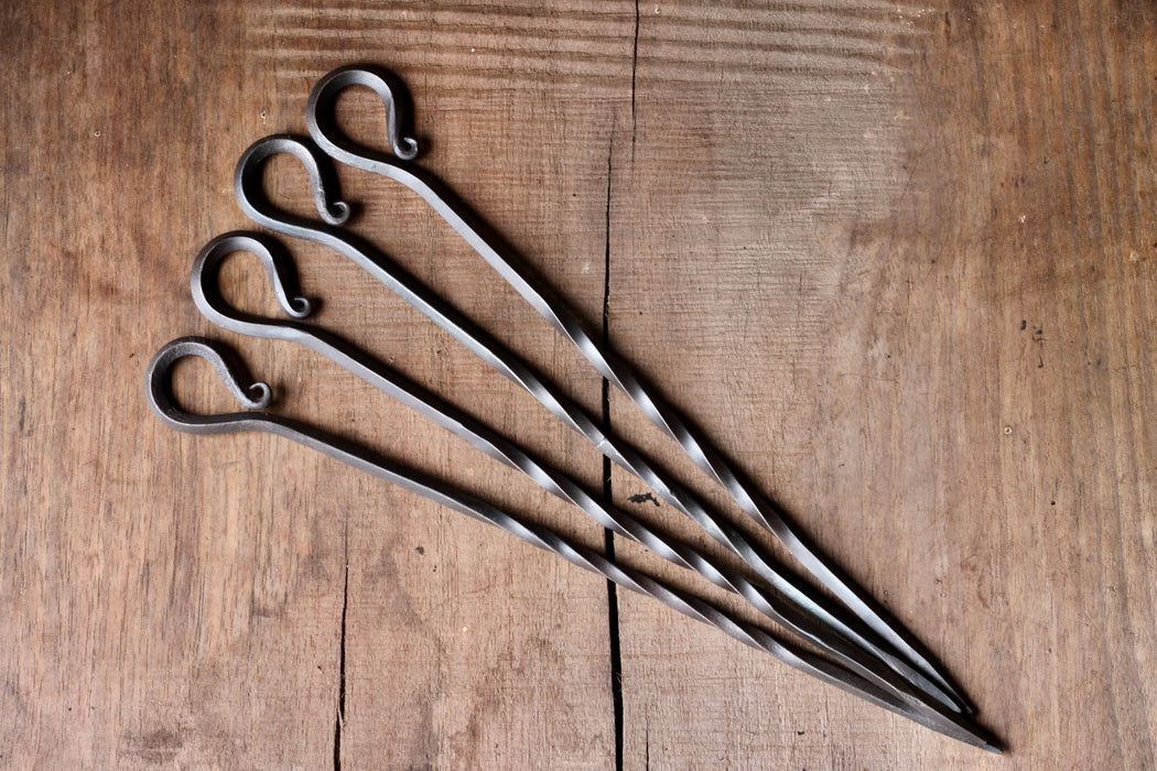 A set of 4 hand forged Skewers on a rustic wooden surface made by Wicks Forge