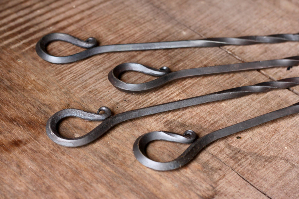 A set of hand forged Skewer handles on a wooden surface by Wicks Forge