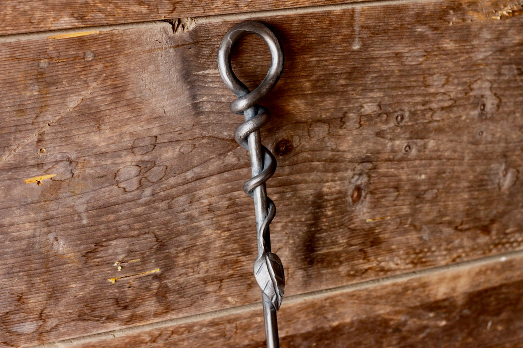 a blacksmith hand forged fire poker with a leaf wrap design by Wicks Forge