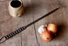 meat flipper made of iron on a wooden table with onions and a ceramic jar on the table 