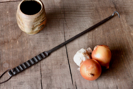 meat flipper made of iron on a wooden table with onions and a ceramic jar on the table 